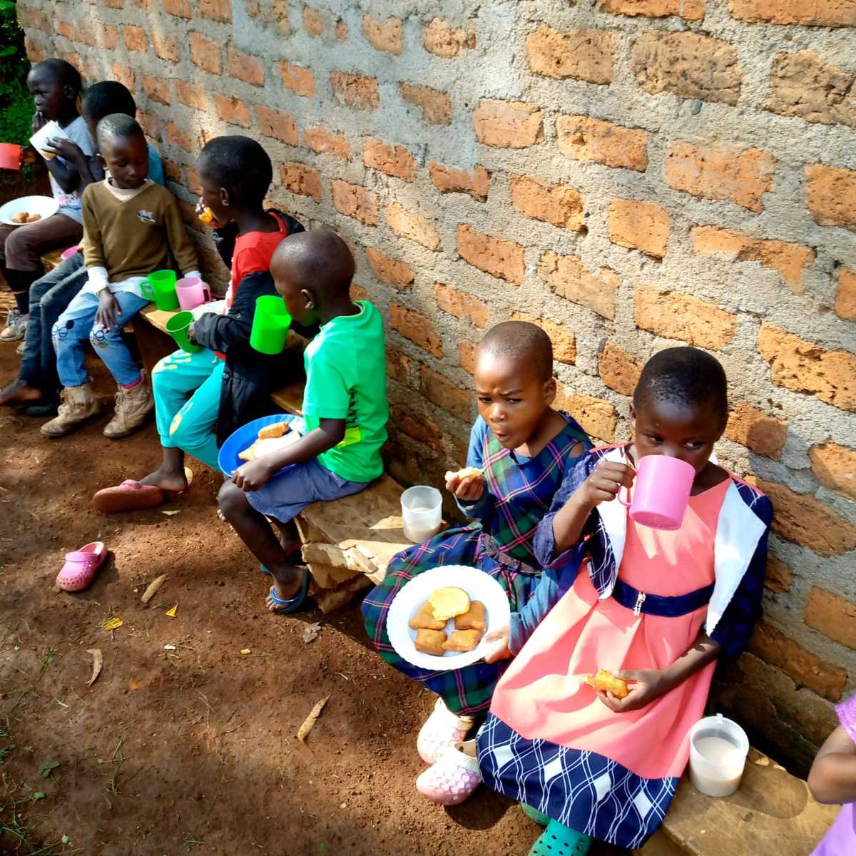 Children sharing a meal beside a brick wall.